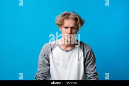 Ernsthafter junger Mann, der intensiv auf die Kamera starrt, auf blauem Hintergrund, fokussierter und konzentrierter Ausdruck Stockfoto