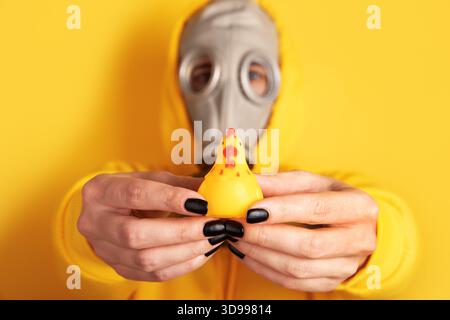 Die Person in Gasmaske und gelbem Hoodie hält das Spielzeug aus Gummi vor einem passenden gelben Hintergrund. Konzeptionelles, auffälliges und auffälliges Bild mit St Stockfoto