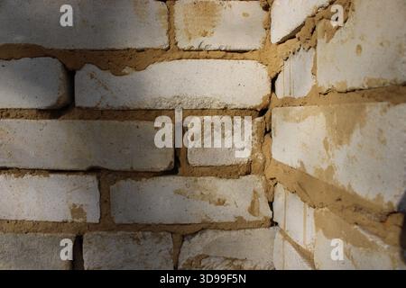 Die Wand aus Ziegeln ist eng dargestellt. Der Mörtel zwischen den Ziegeln hat unterschiedliche Texturen und Farben. Licht leuchtet auf die Wand und hebt den hervor Stockfoto