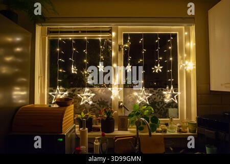Glühende weihnachtslichter und Sterndekorationen hängen in einer gemütlichen Fensterszene Stockfoto