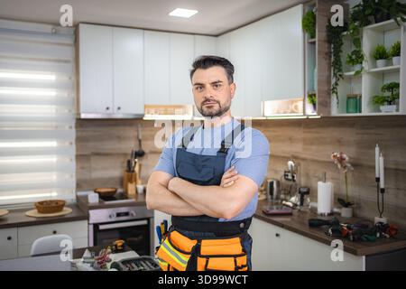 Handwerker, der mit gekreuzten Armen in der Küche steht und in die Kamera blickt Stockfoto