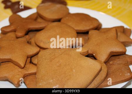 Kekse in verschiedenen Formen wie Sterne und Glocken werden auf einer weißen Platte platziert. Sie sind frisch gebacken und bereit für ein Treffen oder eine Feier im Haus Stockfoto