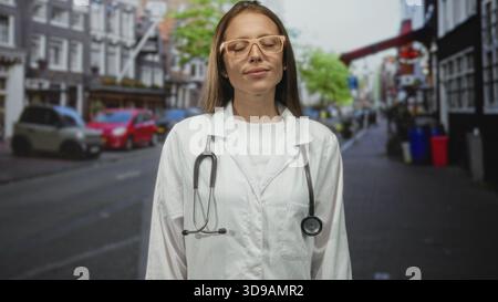 Frau Ärztin mit Stethoskop, Augen geschlossen und leichtes Lächeln auf der Straße in der Stadt; ruhiges Mitgefühl leise Stärke. Stockfoto