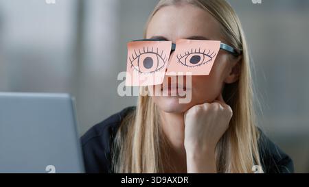 Müde kaukasische Geschäftsfrau tut so, als ob sie einen Laptop mit Haftnotizen und Augen auf die Brille zieht Geschäftsfrau schläfrig weibliches Mädchen tut so, als ob sie arbeitet Stockfoto