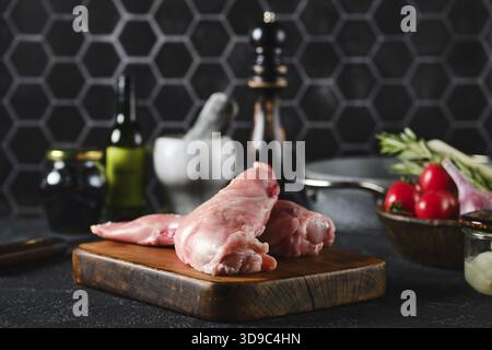 Ein Paar rohe Hasenbeine auf einem hölzernen Schneidebrett, umgeben von Küchenzutaten Stockfoto