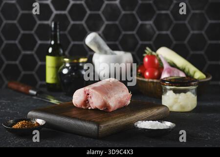 Ein frischer Kaninchen-Sattel auf einem hölzernen Schneidebrett umgeben von frischem Gemüse und Kochutensilien Stockfoto