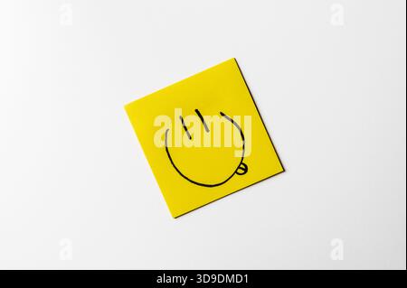 Gelbe Haftnotiz mit einem handgezeichneten Smiley-Symbol auf weißem Hintergrund. Konzeptbild über Glück, positive Stimmung und Emotionen. Stockfoto