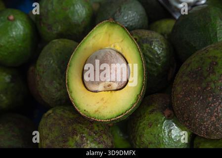 Frische, reife Avocado, in zwei Hälften geschnitten auf einem Haufen Avocados. Gesunde Lebensmittel, Bio-Produkte, tropische Früchte, natürlicher Markt Stockfoto