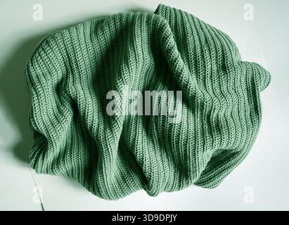 Strukturiertes Foto von zerknittertem, grobem Strickstoff, Pullover, Schal in einem weichen Salbeigrün auf hellem Hintergrund. Symbol für Komfort, Gemütlichkeit, Fashi Stockfoto