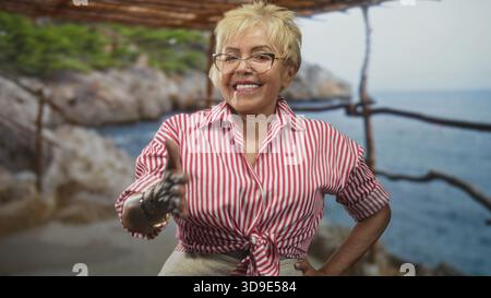 Die ranghöchste hispanische Frau streckt die rechte Hand für den Handschlag aus, trägt ein rot gestreiftes Hemd und Armbänder unter einer Pergola an der felsigen Küste; freundliche Begrüßung. Stockfoto