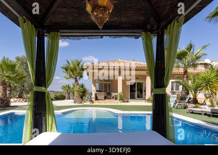 Die luxuriöse Villa sieht man vom Himmelbett in der Nähe des Pools mit Palmen und sonnigem Himmel. Stockfoto