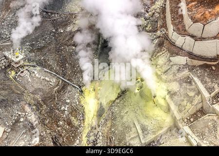 Ein Fumarolenfeld mit schwefelgelben Ablagerungen und einer Dampfkontrollstation im Owakudani-Krater, Hakone, Kanagawa, Japan. Die gelben Bereiche zeigen Zonen an, in denen elementarer Schwefel direkt aus den aufsteigenden Gasen kondensiert und ausfällt. Links im Bild befindet sich die Dampfablassstation mit ihrem Metallgerüst Stockfoto
