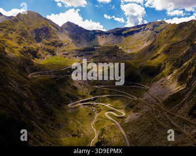 Aus der Vogelperspektive auf die gewundene Transfagarasan-Straße, die sich durch die zerklüfteten, grünen Berge unter einem Himmel mit flauschigen Wolken schlängelt, Curtea de Arges, J Stockfoto