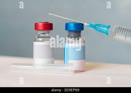 Arzneimittelkonzept mit Spritze und Impfstofffläschchen mit Flüssigkeit. Die Arzneimittelflasche hat einen leeren blauen Copyspace. Herstellung von Impfstoffen Stockfoto