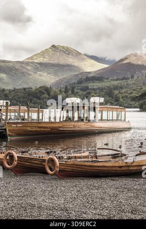 Blick auf hölzerne Boote, die ruhig auf dem ruhigen See schweben und die majestätischen Berge unter einem bewölkten Himmel reflektieren, Lake District, England, Vereinigtes Königreich Stockfoto