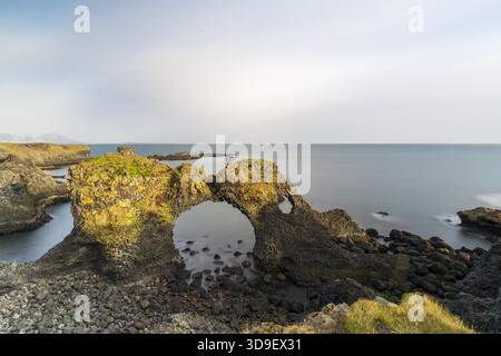 Blick auf die Felsformation Gatklettur, die trotzig gegen das türkisfarbene Meer steht, in goldenes Sonnenlicht getaucht, eine zerklüftete Landschaft in Arnarstapi, Sn Stockfoto