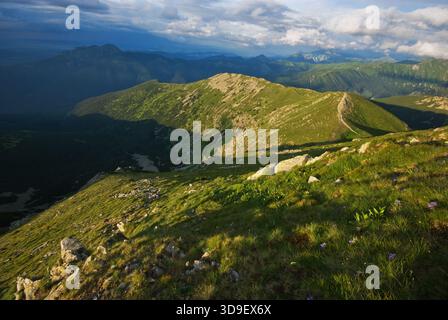 Der Blick auf sanfte grüne Hügel und zerklüftete Berggipfel unter einem dramatischen Himmel schafft einen lebendigen Wandteppich aus Licht und Schatten, Partizanska Lupca, Zilinsky Stockfoto