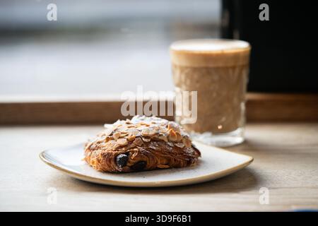 Schokoladenmandelcroissant und ein Glas Kaffee auf einem Kaffeetisch Stockfoto