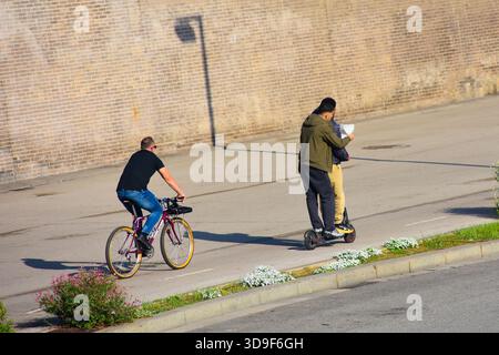 Zwei junge Männer, die einen Elektroroller fahren. Der Co-Pilot gibt Anweisungen, die er von einem Blatt Papier liest, das er in der Hand hält. Stockfoto