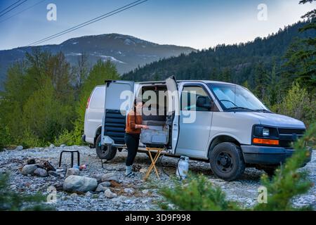 Frau kocht auf tragbarem Grill vor dem Wohnmobil in den Bergen Stockfoto