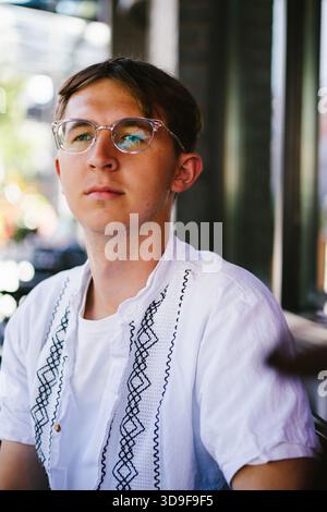 Ein junger Mann mit Brille sitzt am Straßenrand in der Stadt Stockfoto