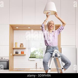 Frau, die auf einer Leiter sitzt und eine Glühbirne in eine Pendelleuchte steckt Stockfoto