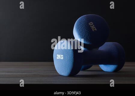 Sportkonzepte mit zwei blauen Neopren-Kurzhanteln auf einem Holztisch und dunkel isoliertem Hintergrund mit hohem Kontrast. Vorderansicht. Stockfoto