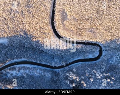 Blick aus der Vogelperspektive auf die Winterlandschaft mit schneebedeckten Berghügeln und gewundenen Waldstraßen am Morgen Stockfoto