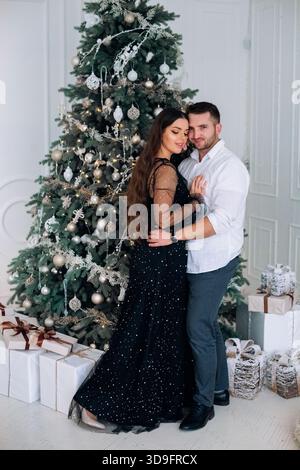 Ein Paar steht nahe beieinander und lächelt vor einem wunderschön geschmückten Weihnachtsbaum. Stockfoto