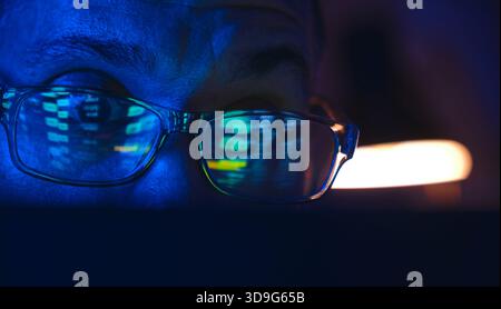 Die Brille einer Person, die digitale Börsendaten von einem Bildschirm in dunkler Umgebung reflektiert Stockfoto