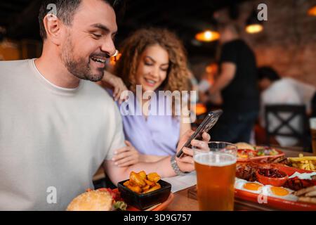 Ein Paar lacht und benutzt das Smartphone beim Mittagessen im Restaurant Stockfoto