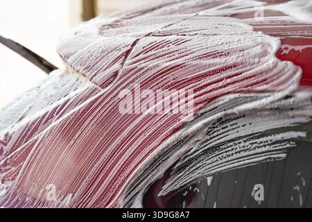 Weiße Seife und Schaumstoff Striche auf roten Platten des Autos gewaschen in selbst dienen Autowäsche, Nahaufnahme Detail Stockfoto