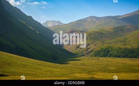 Weite Aussicht auf ein friedliches, grünes Tal, umgeben von Bergen und felsigen Klippen im Nordkaukasus nahe Mount Elbrus an einem klaren, sonnigen Tag Stockfoto
