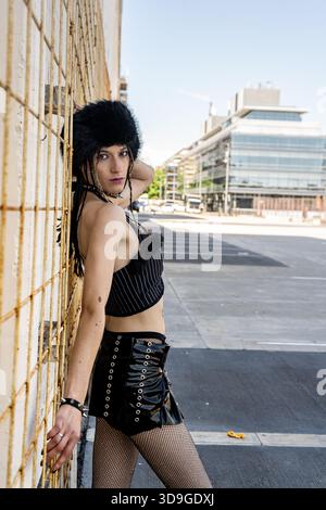 Junge Frau in alternativer Mode, mit Pelzmütze, Vinylrock und Netzstrümpfen auf einer städtischen Straße Stockfoto