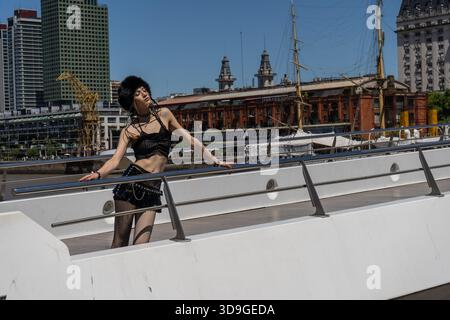 Junge Frau in alternativer dunkler Mode und Hut posiert am Hafen von puerto madero, buenos aires, trendiger urbaner Gothic-Stil, Sommertageslicht Stockfoto