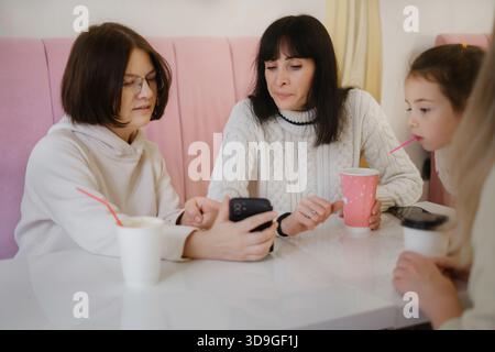 Weibliche Kollegen sitzen im Café, trinken Kaffee und diskutieren über Projekte, während sie Ideen auf dem Smartphone-Bildschirm austauschen und gemeinsam arbeiten Stockfoto