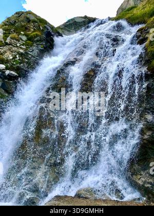 Ein dynamischer Gebirgsbach fließt wie ein kleiner Wasserfall über eine imposante Felswände am Mattmark-Stausee über SaaS-Fee, Wallis, Schweiz Stockfoto
