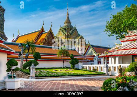 Außenansicht des Wat Pho mit reich verzierten Stupas bedeckt mit farbenfroher Blumenkeramik und goldenen Tempeldächern, die unter einem klaren blauen Himmel auf A leuchten Stockfoto