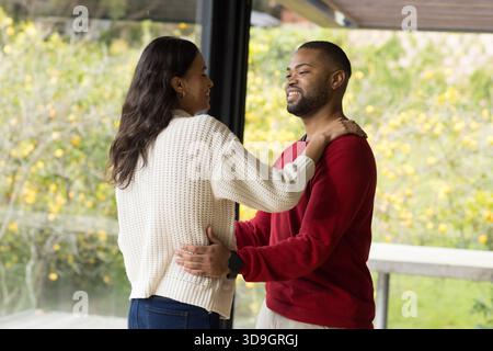 Verschiedene Paare, die sich auf einer modernen Veranda durch eine Glaswand mit Geländer mit Blick auf gelbe Bäume umschließen Stockfoto