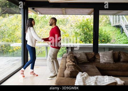 Verschiedene Paare halten Hände neben einer Glasschiebetür im Wohnzimmer mit Blick auf Terrasse und Garten Stockfoto
