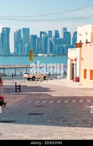 Mina District am alten Hafen von Doha in Katar: 15. März 2025. Eine sonnendurchflutete Uferpromenade umrahmt eine moderne Skyline der Stadt hinter ruhigen Gewässern. Beigefarbener stuck Stockfoto