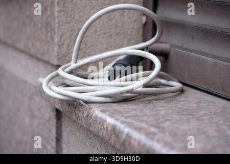 Ein weißes Stromkabel liegt auf einem Steinvorsprung, was auf das städtische Leben hindeutet. Stockfoto