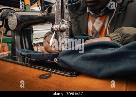 Nahaufnahme der Hände, die Stoff mit einer Vintage-Nähmaschine nähen, mit detaillierten Schneiderarbeiten, Handwerkskunst und Textilreparatur in einem kleinen Handwerksauftrag Stockfoto