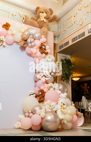 Üppiger Bogen aus rosa, weißen und silbernen Ballons, die mit Plüschteddybären verziert sind, dekorieren einen Innenraum für eine Fotozone oder ein Kinderfest Stockfoto