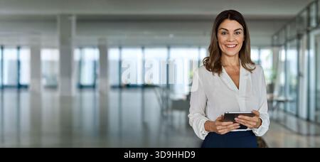 Glückliche, reife Geschäftsführerin, die im Büro ein Tablet hält. Hochformat. Stockfoto