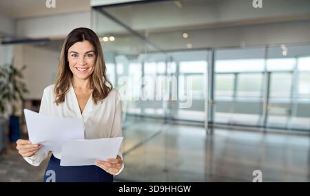 Glückliche lateinische professionelle Geschäftsfrau mittleren Alters, die Papiere im Büro hält. Stockfoto