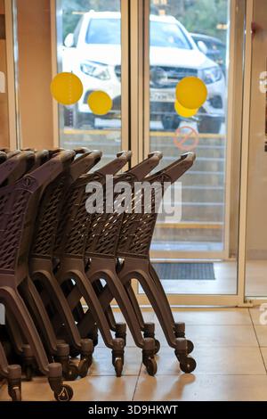Nahaufnahme von gestapelten Kunststoff-Einkaufswagen im Supermarkt durch Glastüren mit Außenansicht und kreisförmigen gelben Aufklebern Stockfoto