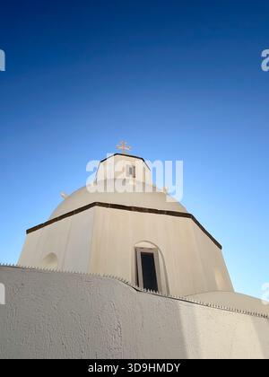 Ein weißes, klassisches griechisches Gebäude mit Blick auf ein traditionelles Inseldorf unter einem hellblauen Himmel, symbolisiert einen Urlaubsort. Stockfoto