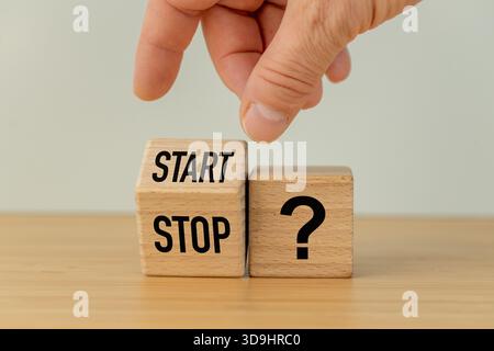 Start- und Stoppsymbol und ein Fragezeichen. Eine Hand, die einen Holzblock dreht, mit den Worten Start, Stopp. Geschäftskonzept. Treffen von Geschäftsentscheidungen, Fortsetzung Stockfoto