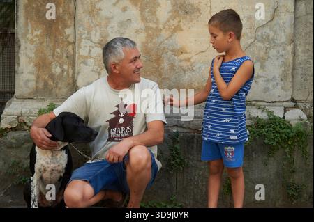 Vater und Sohn mit ihrem Hund auf der Straße in Pescia, Italien, interagieren, während eine Parade vorbei geht. Stockfoto